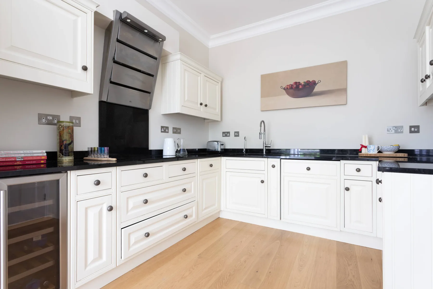 A bright kitchen with white cabinets, black countertops, and a wooden floor.