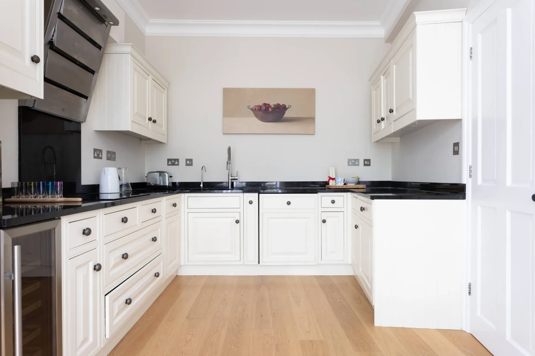 A bright kitchen with white cabinets, dark countertops, and a light wood floor.