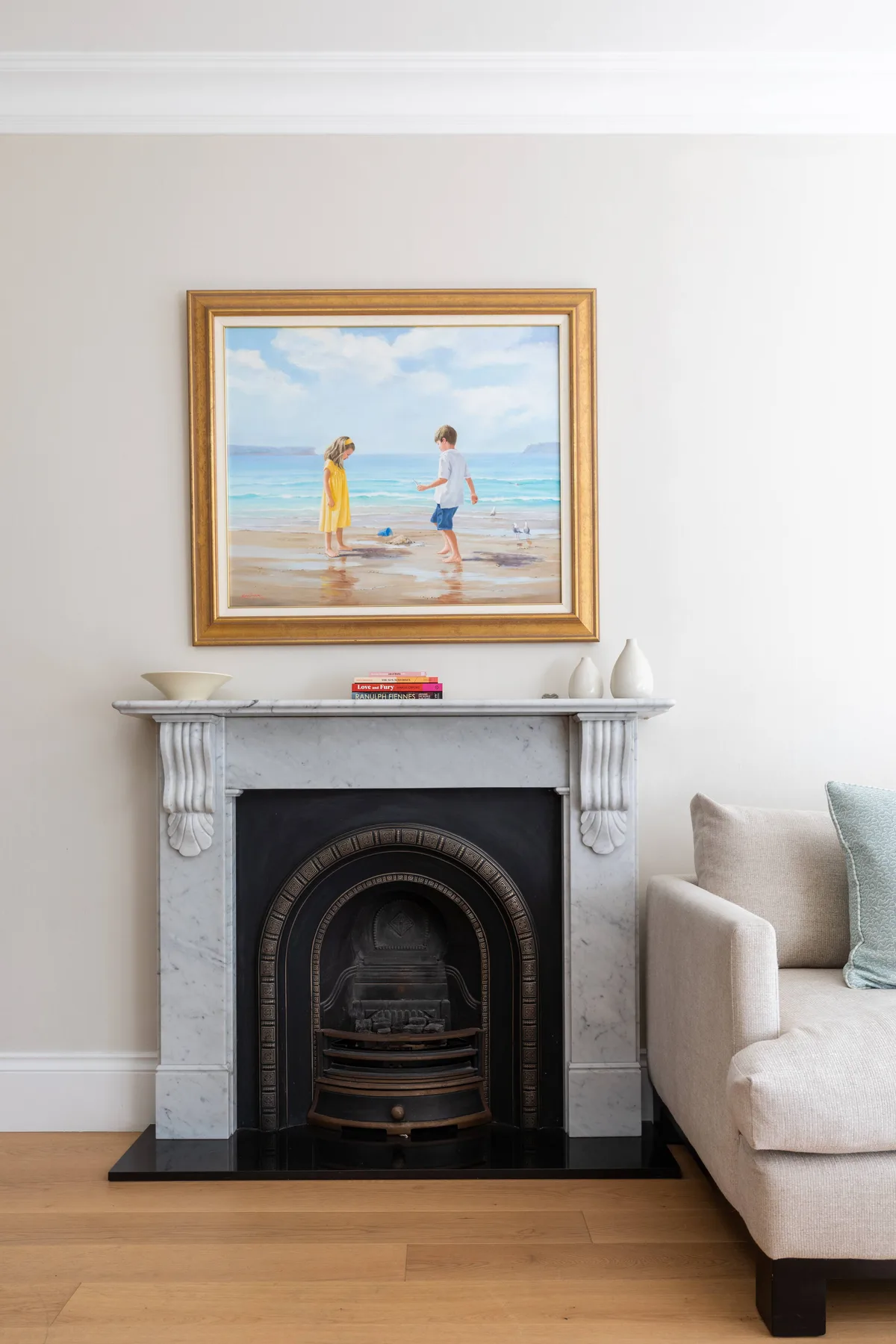 A living room with a fireplace and a framed beach scene above it.