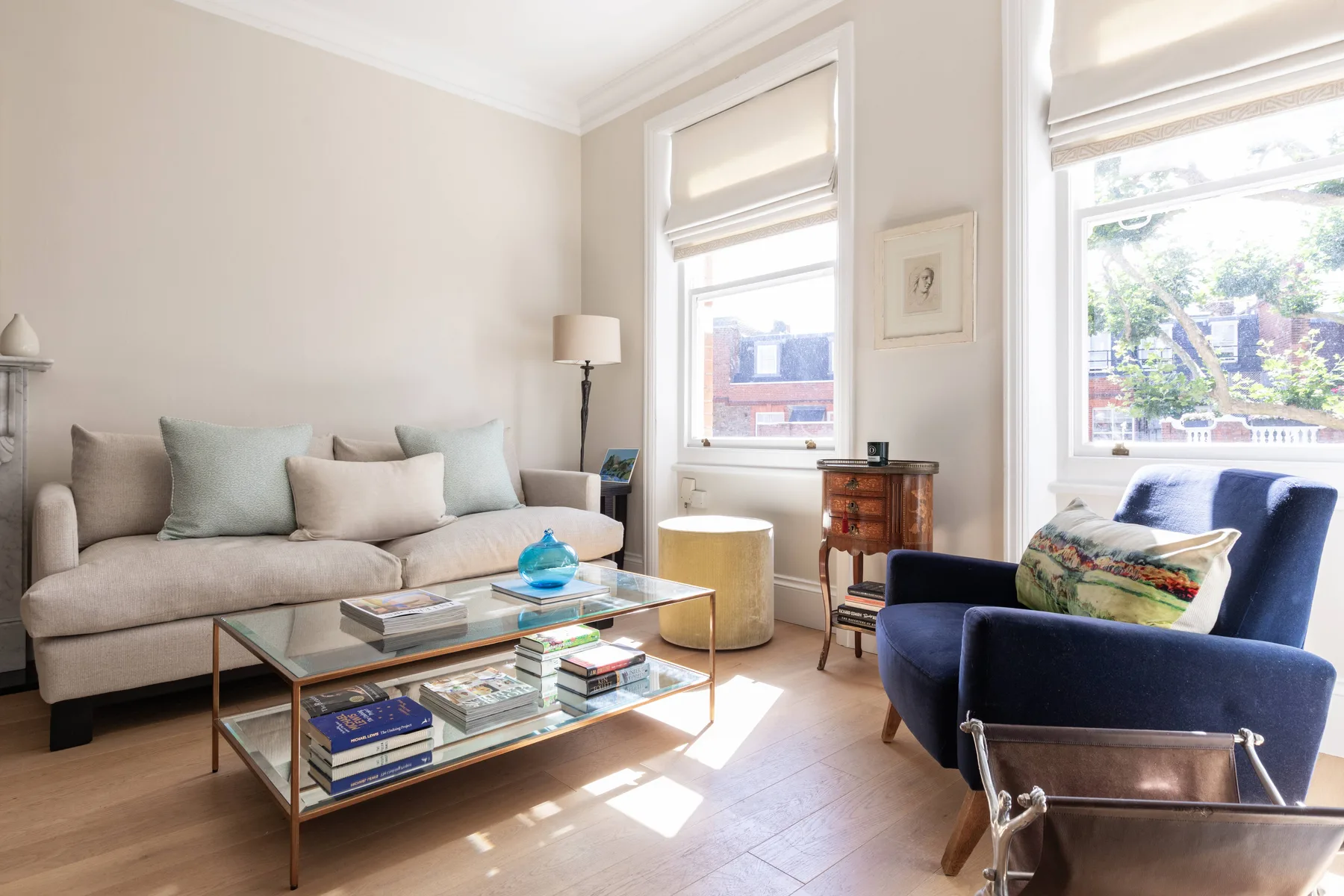 A bright living room with a sofa, glass coffee table, and blue armchair.