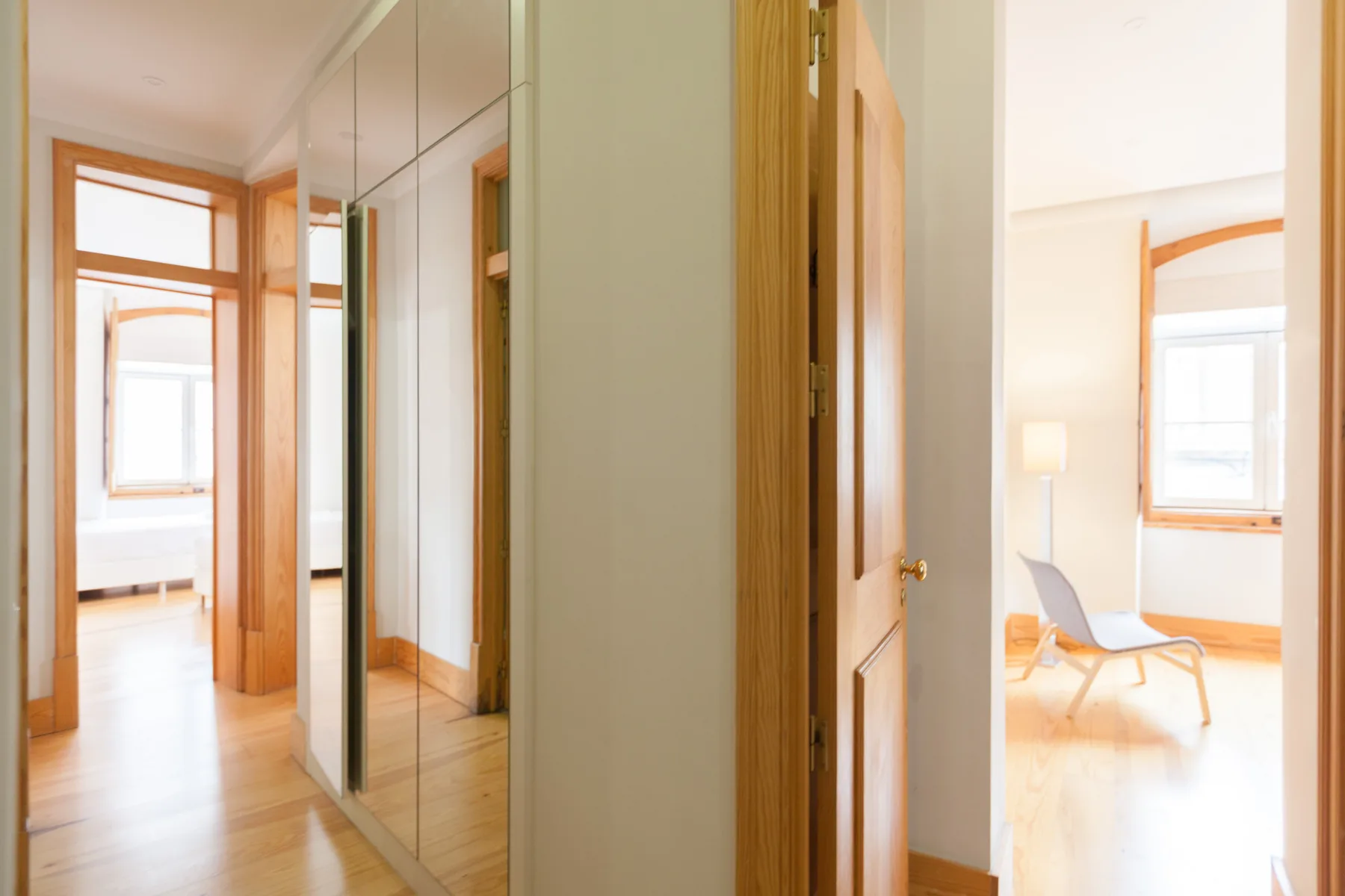 Pasillo luminoso de apartamento con puertas de armario espejadas y una puerta abierta.