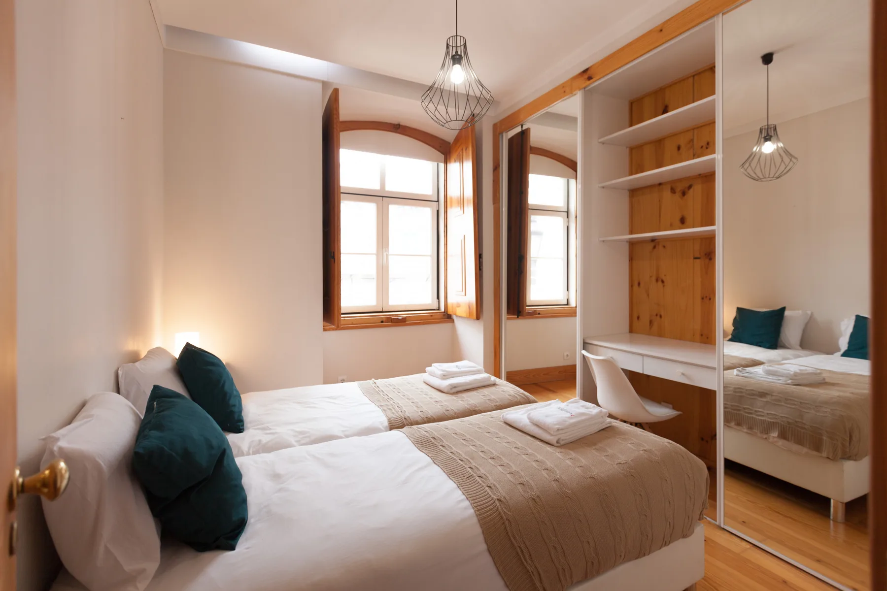 Un dormitorio luminoso con dos camas, una ventana y estanterías de madera integradas.