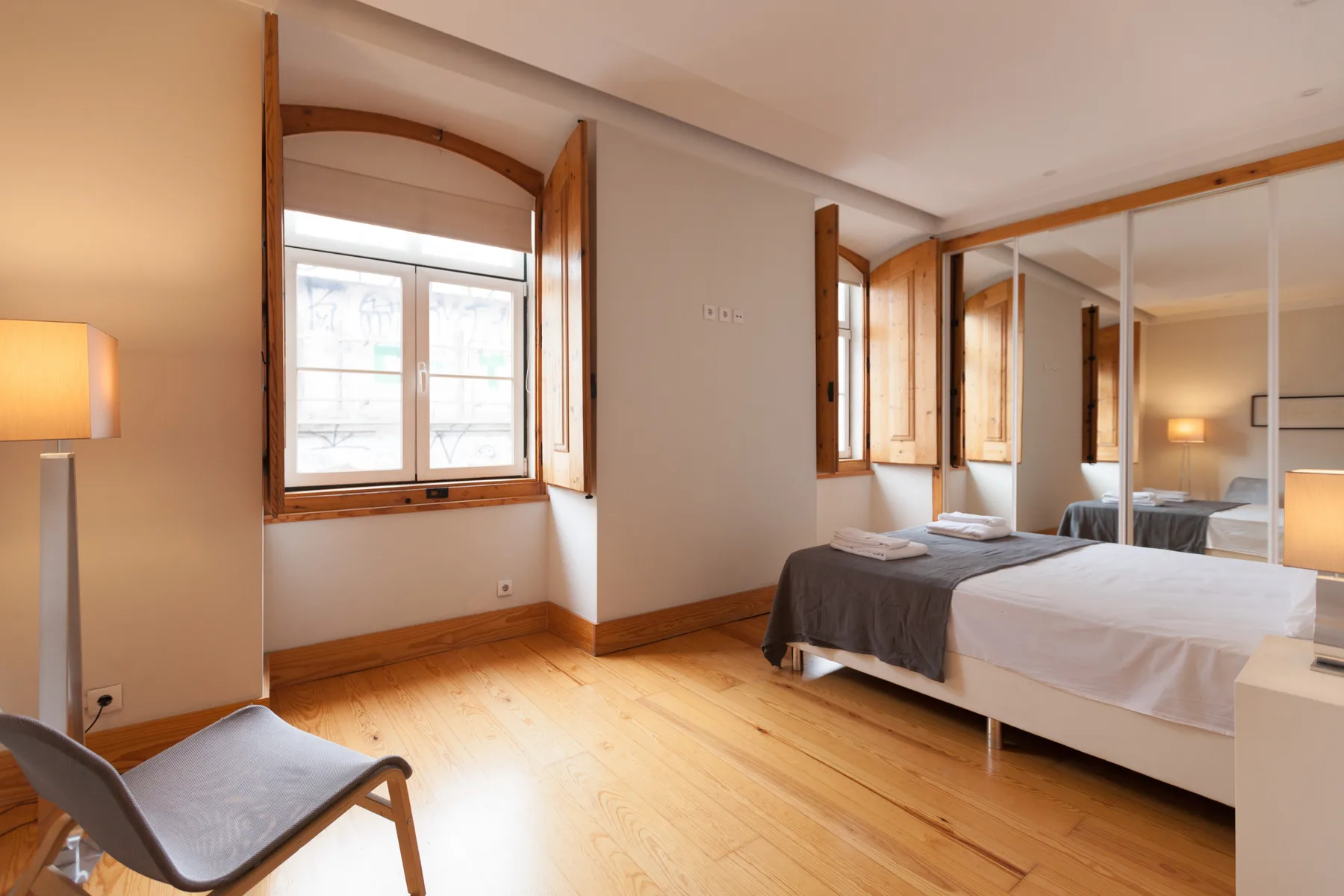 Dormitorio con una cama, puertas de armario con espejo y suelo de madera.