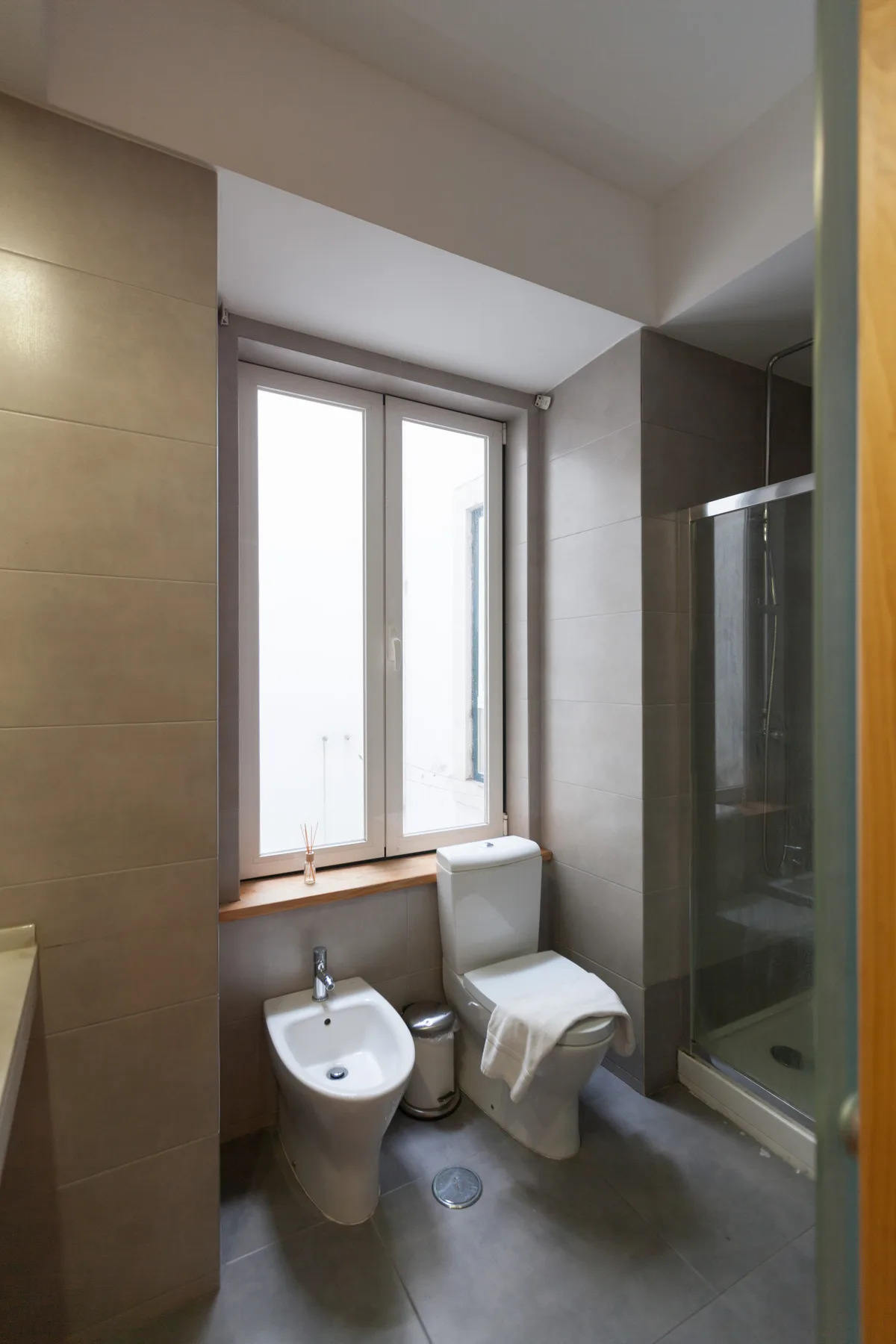 Un baño con inodoro, bidé y ducha de vidrio junto a una ventana.