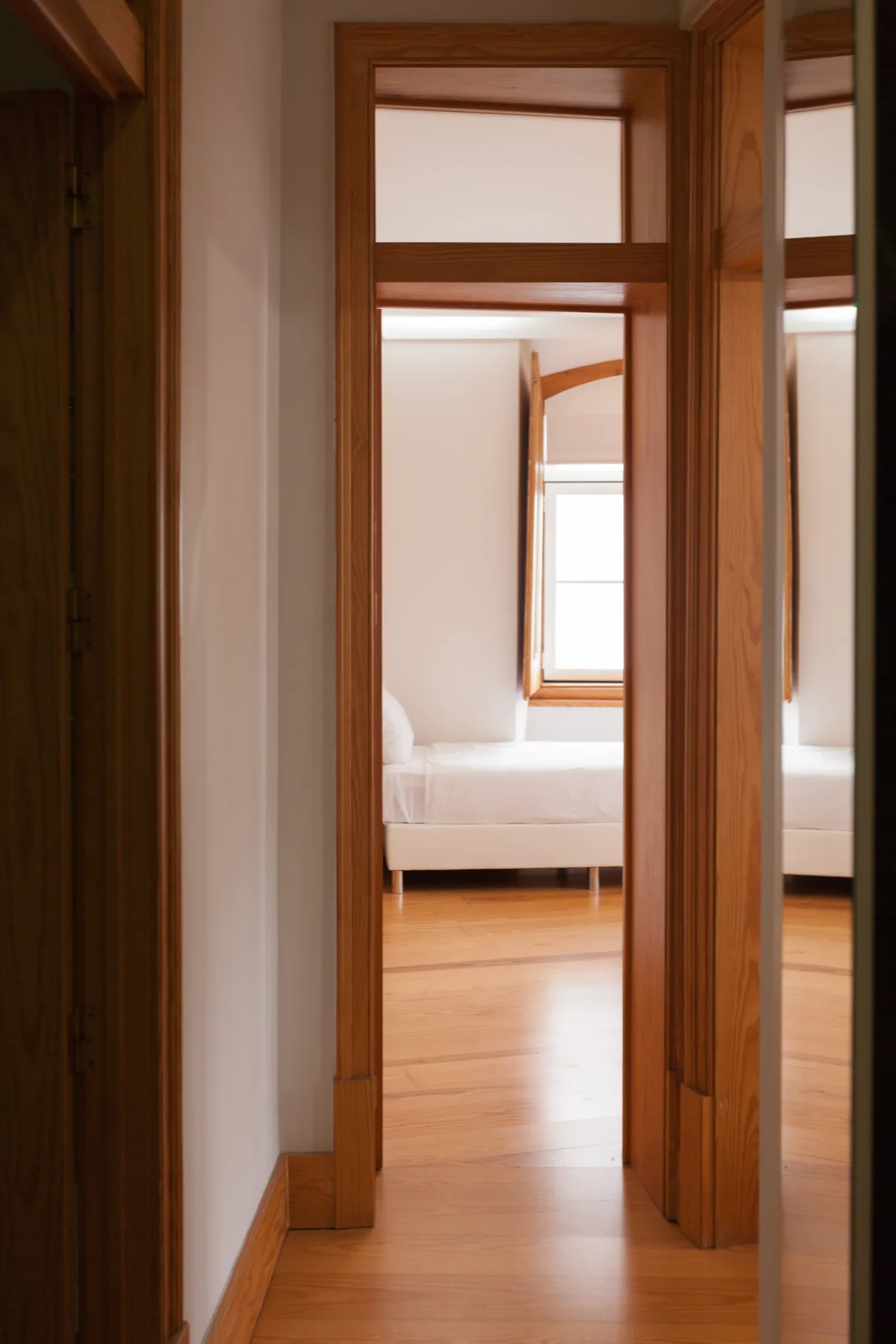 Se ve un dormitorio a través de una puerta de madera, con una cama bajo una ventana.