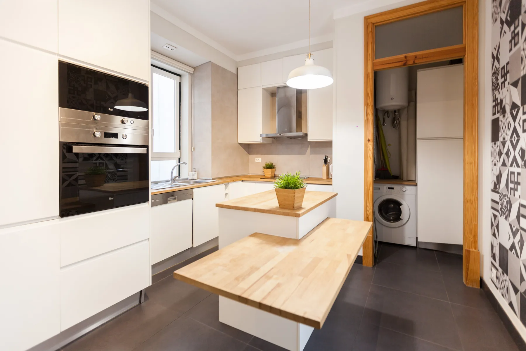 Una cocina luminosa con armarios blancos y una encimera central de madera.