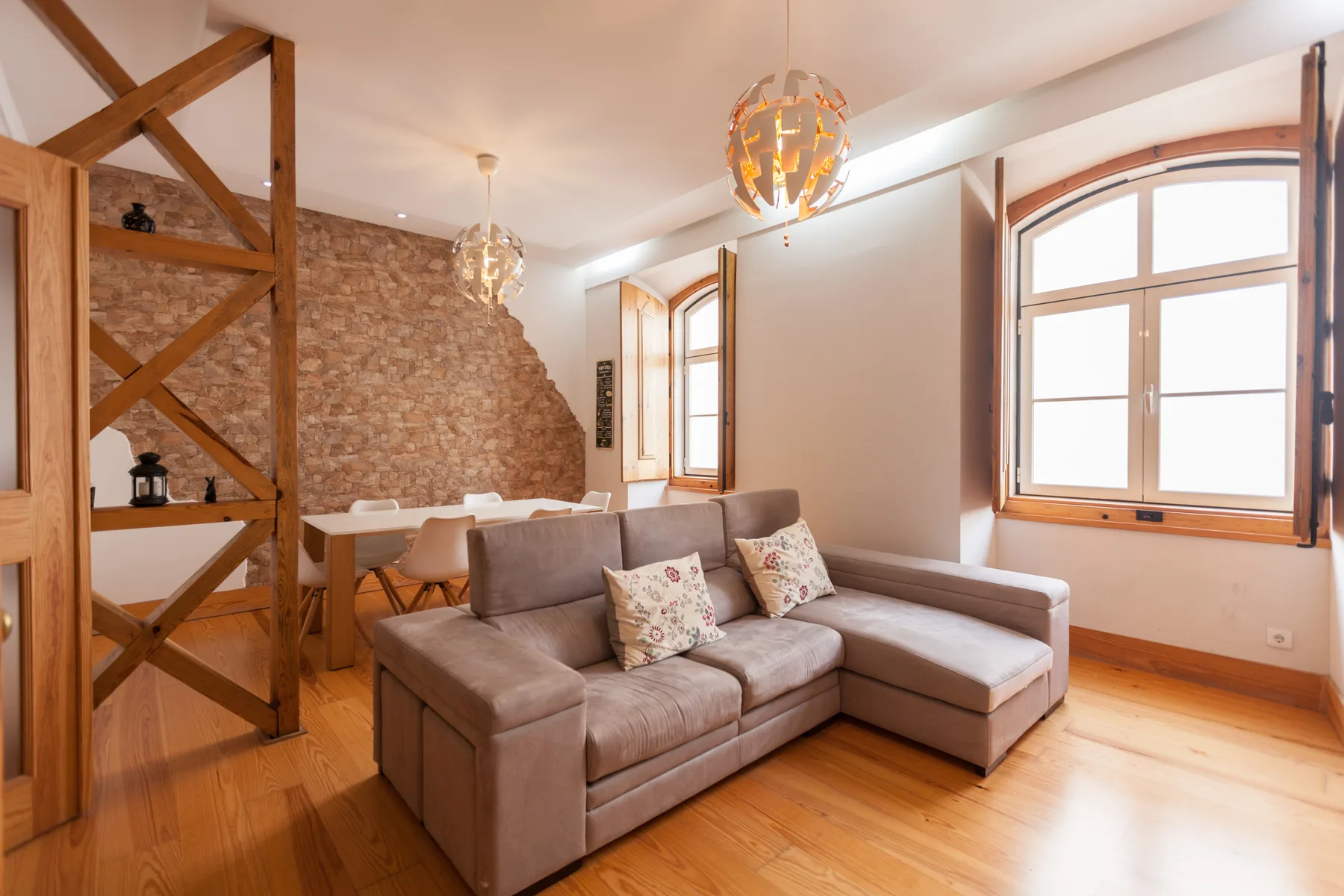 Una sala de estar con un sofá seccional, suelo de madera y ventanas grandes.
