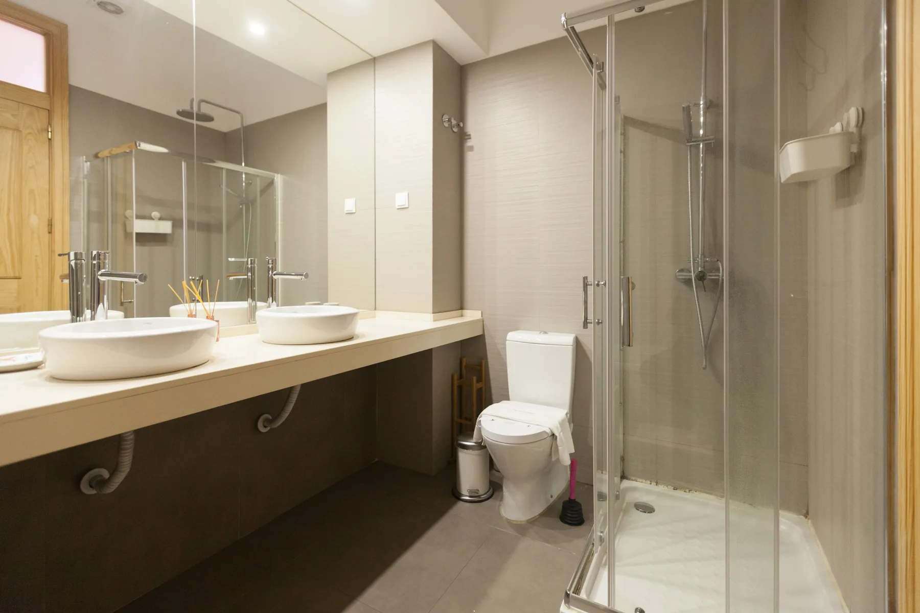 Un baño con un lavabo largo, lavabos, un inodoro y una ducha de vidrio.