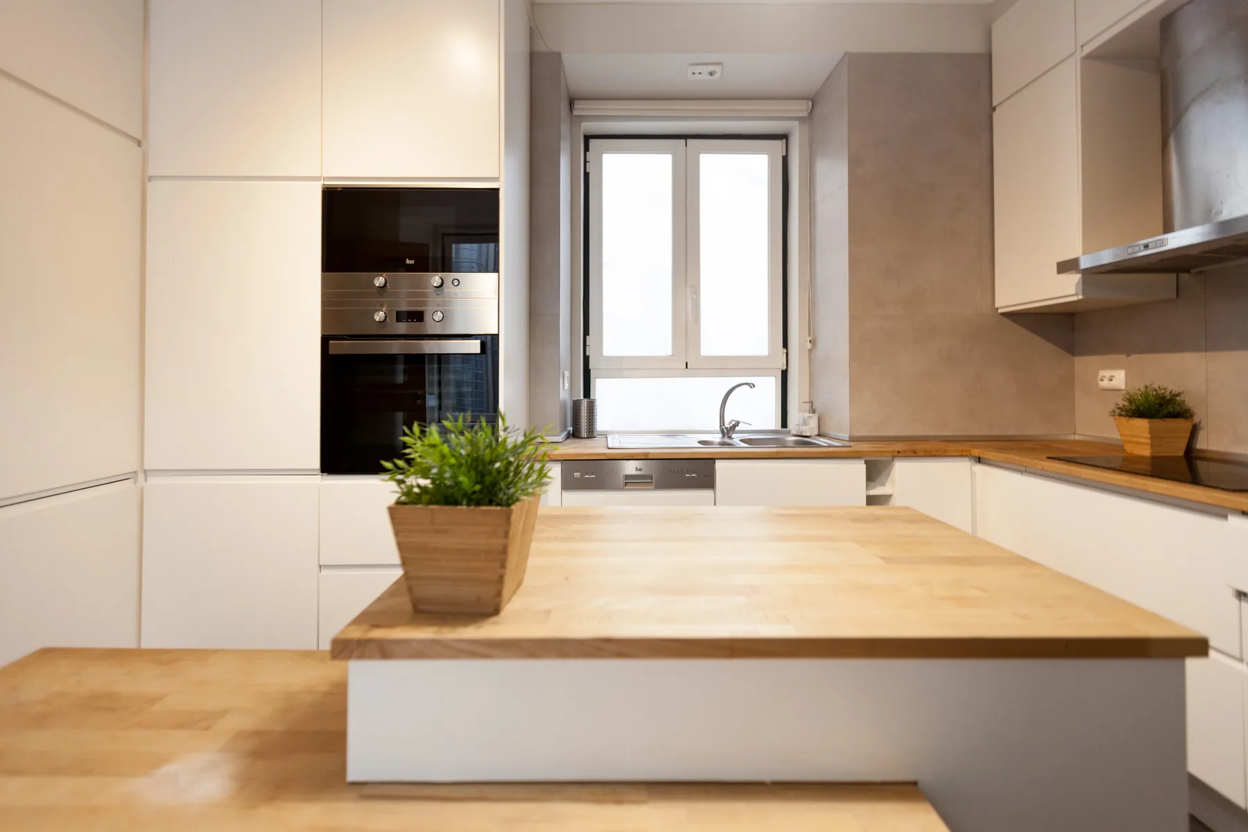 Una cocina luminosa tiene gabinetes blancos, una isla de madera y una ventana sobre el fregadero.