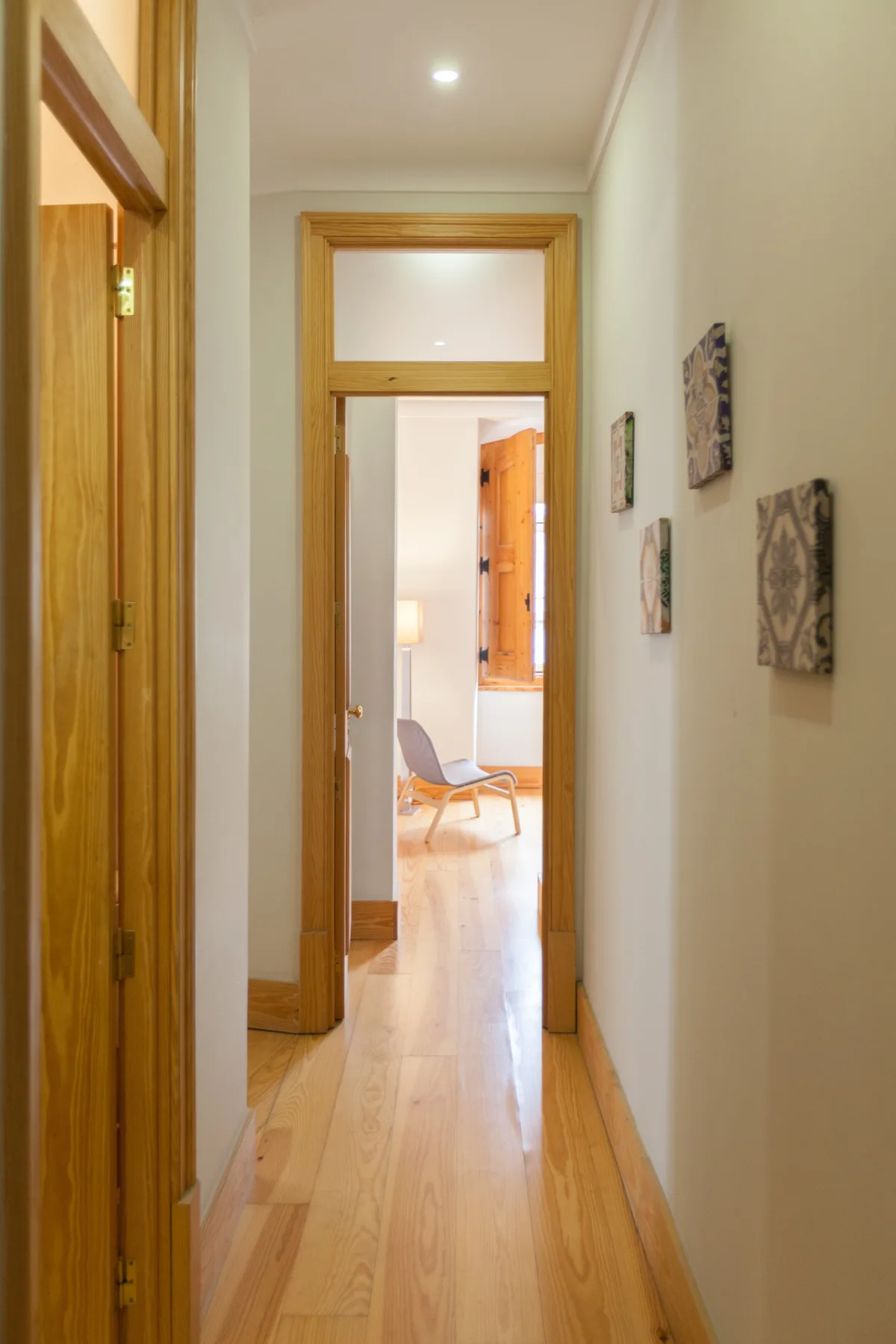 Un pasillo con suelo de madera y una puerta abierta que da a una habitación luminosa.