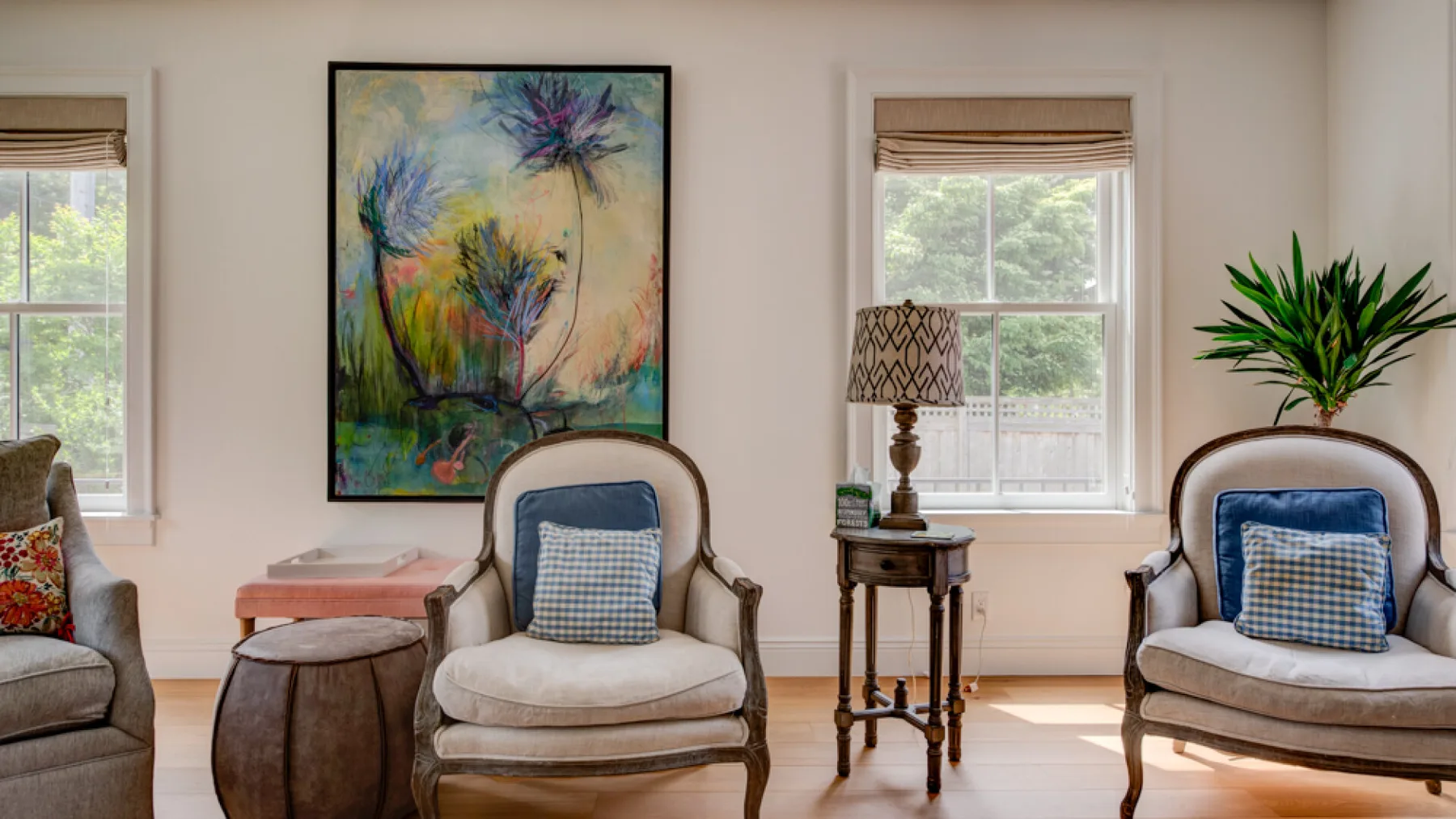 A bright sitting room with cushioned seating, side tables, and colorful wall art.