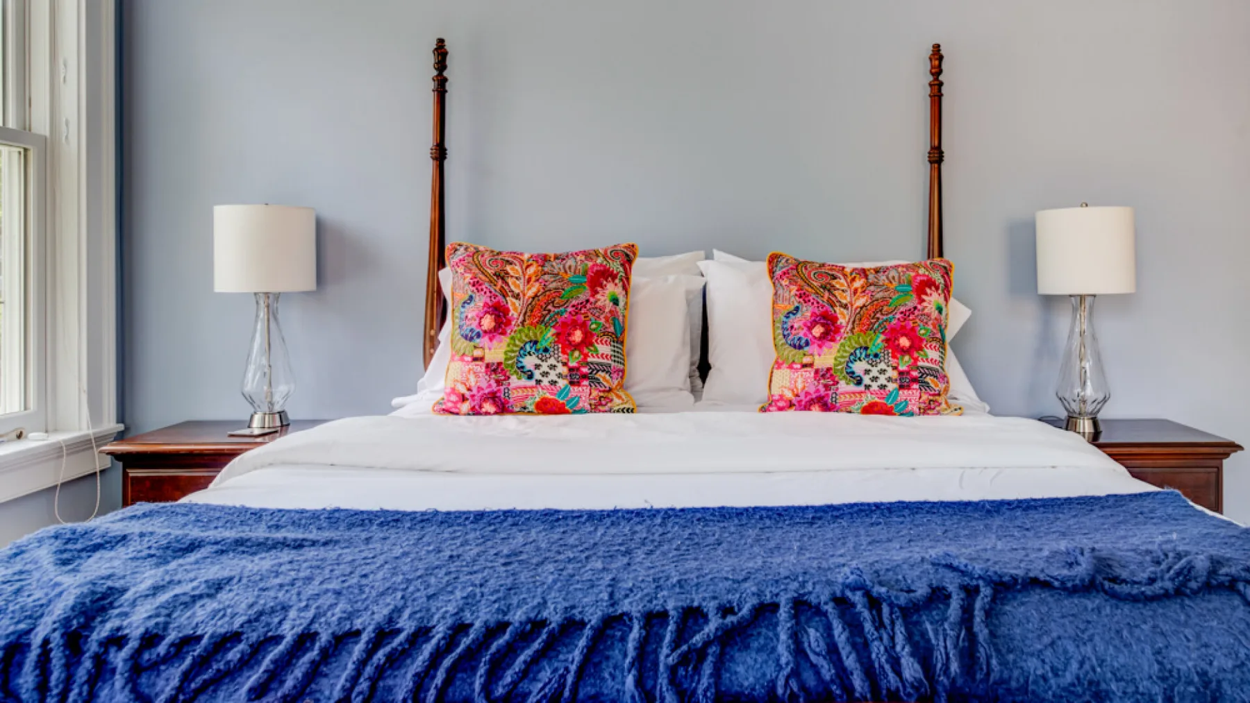 A bedroom with a bed dressed in white linens and colorful floral pillows.