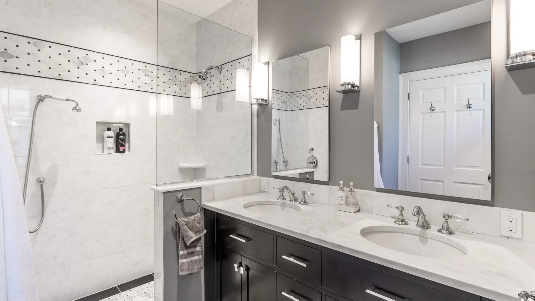 A bright bathroom with a glass shower and a long double-sink vanity.