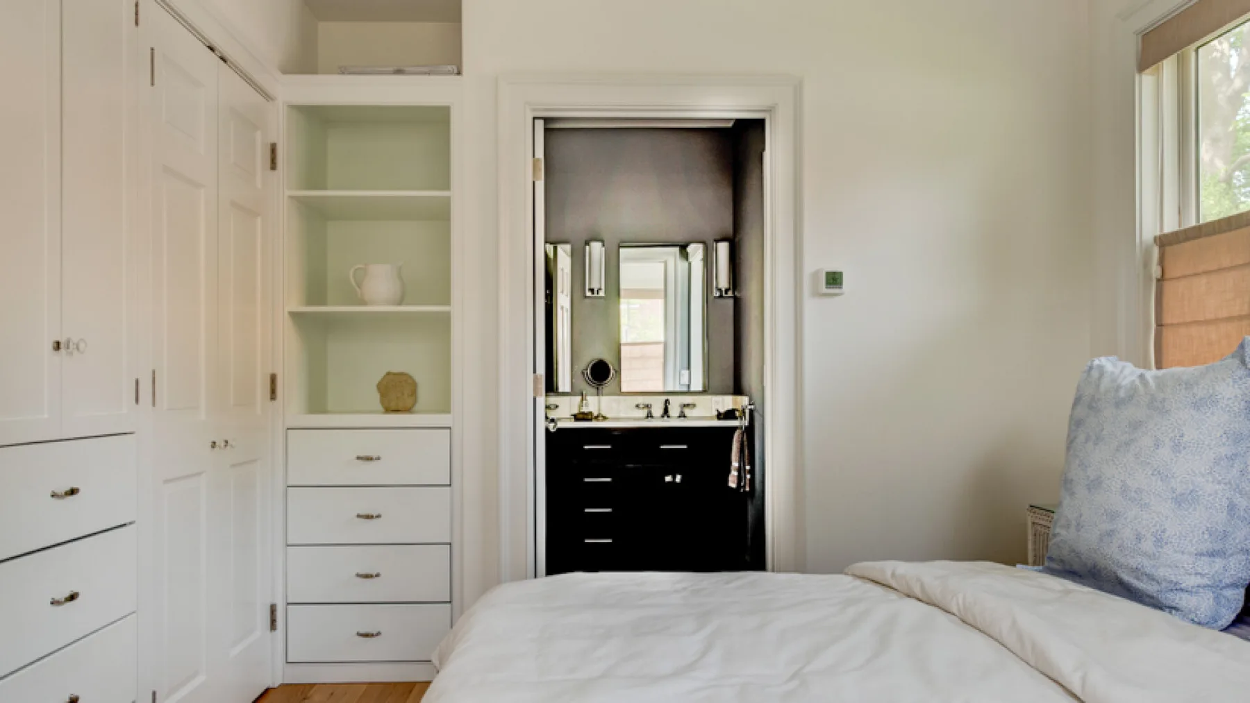 A bedroom with a bed beside built-in shelves and an open bathroom doorway.