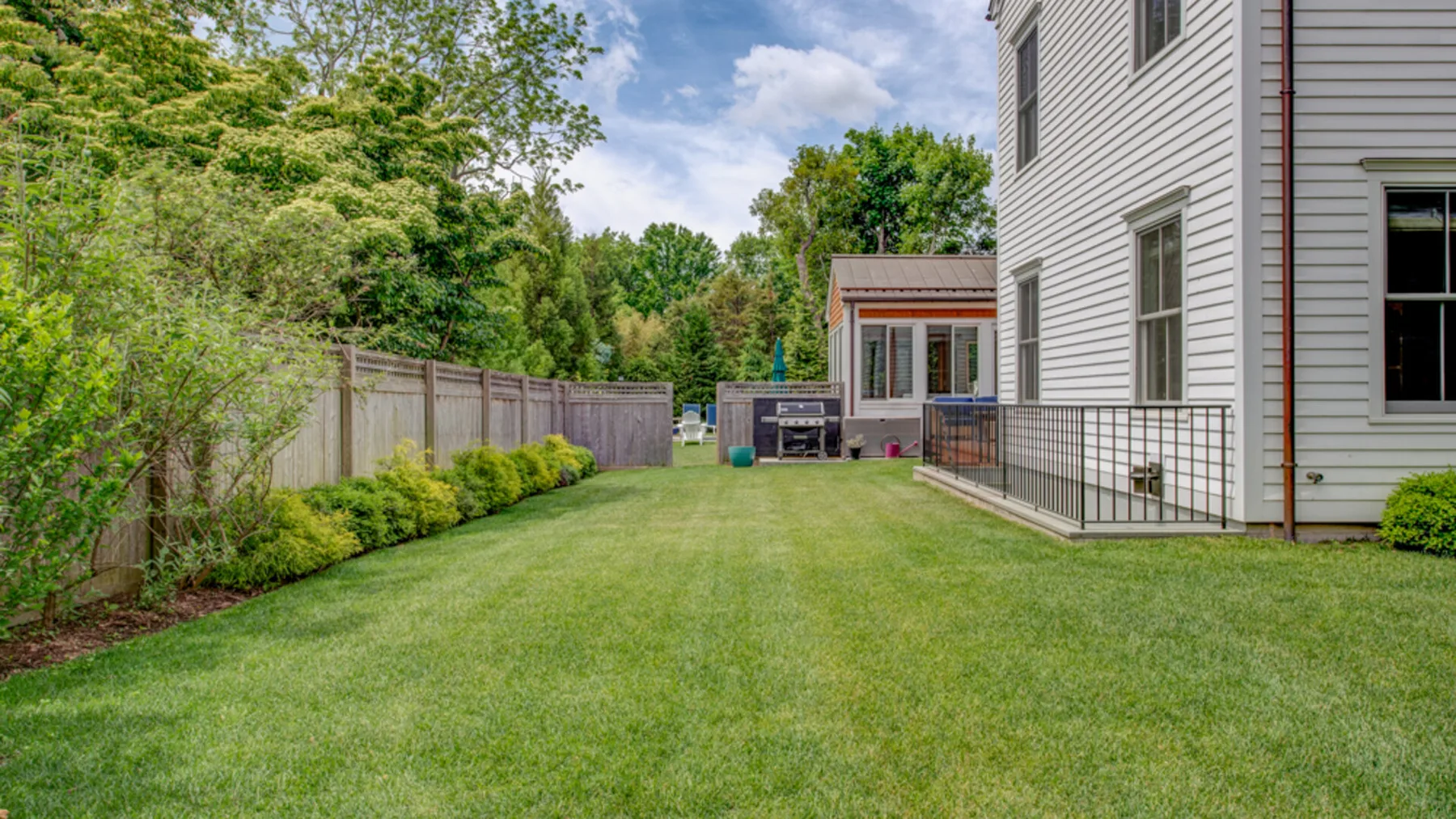 A green lawn beside a house, with trees and a fenced patio in the background.