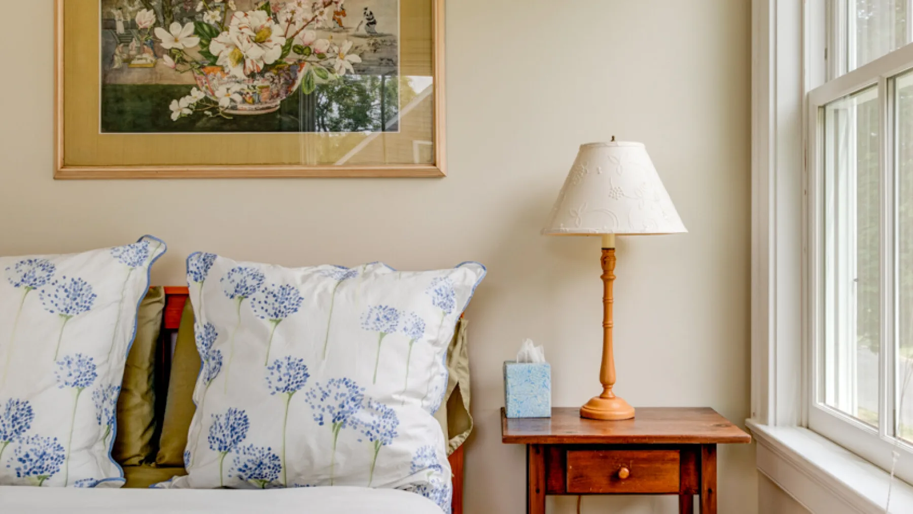 A bright sitting area with floral cushions beside a wooden side table and window.