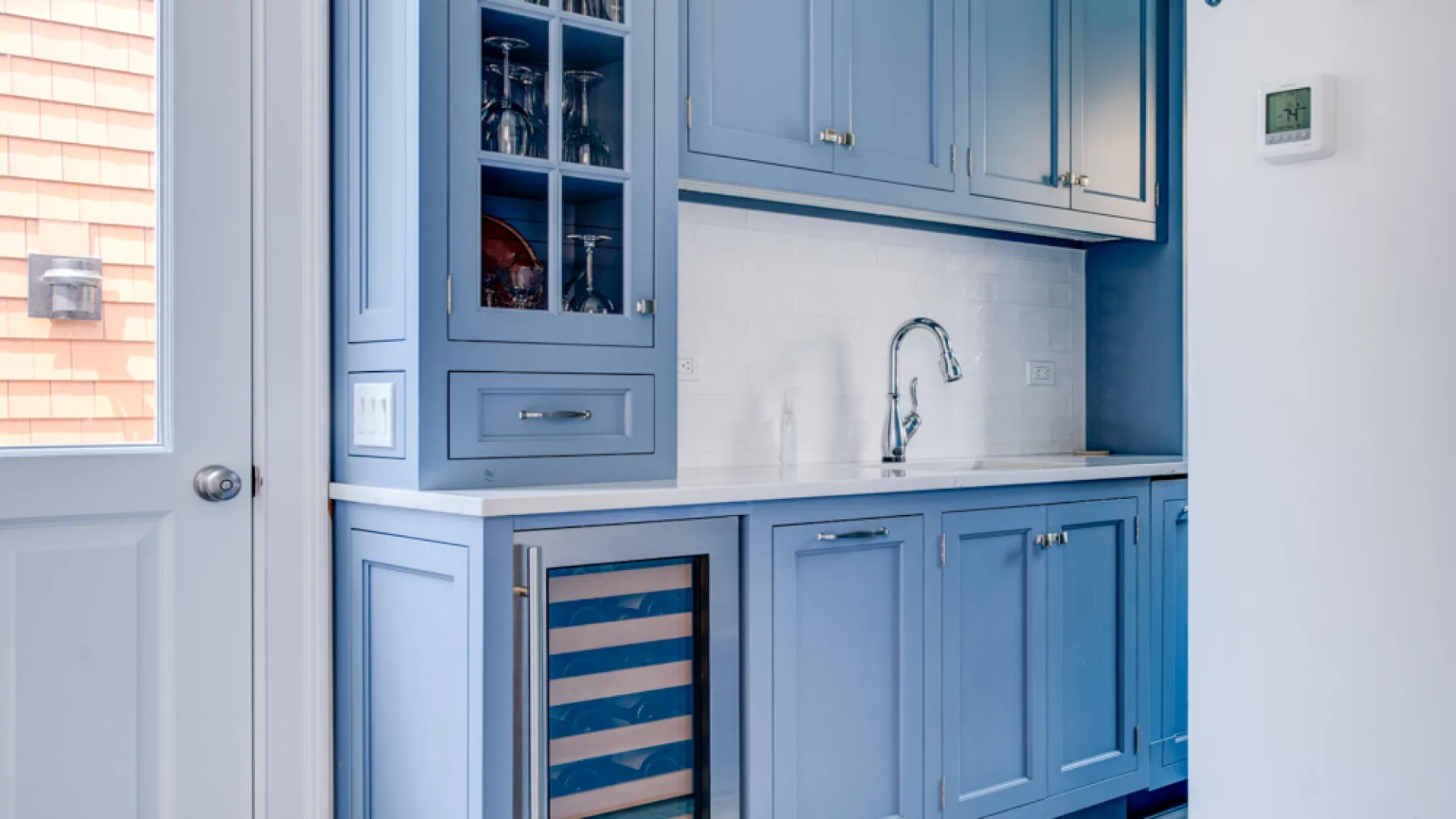 A blue kitchen cabinet area with a countertop, sink, and glass-fronted beverage cooler.