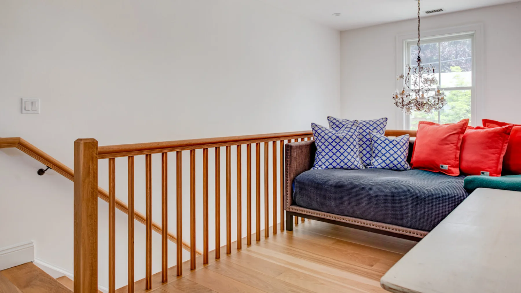 A bright upstairs landing has a cushioned seating area beside a wooden railing.