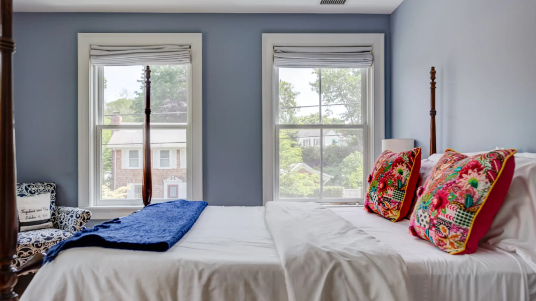 A bedroom with a bed, colorful pillows, and two large windows.