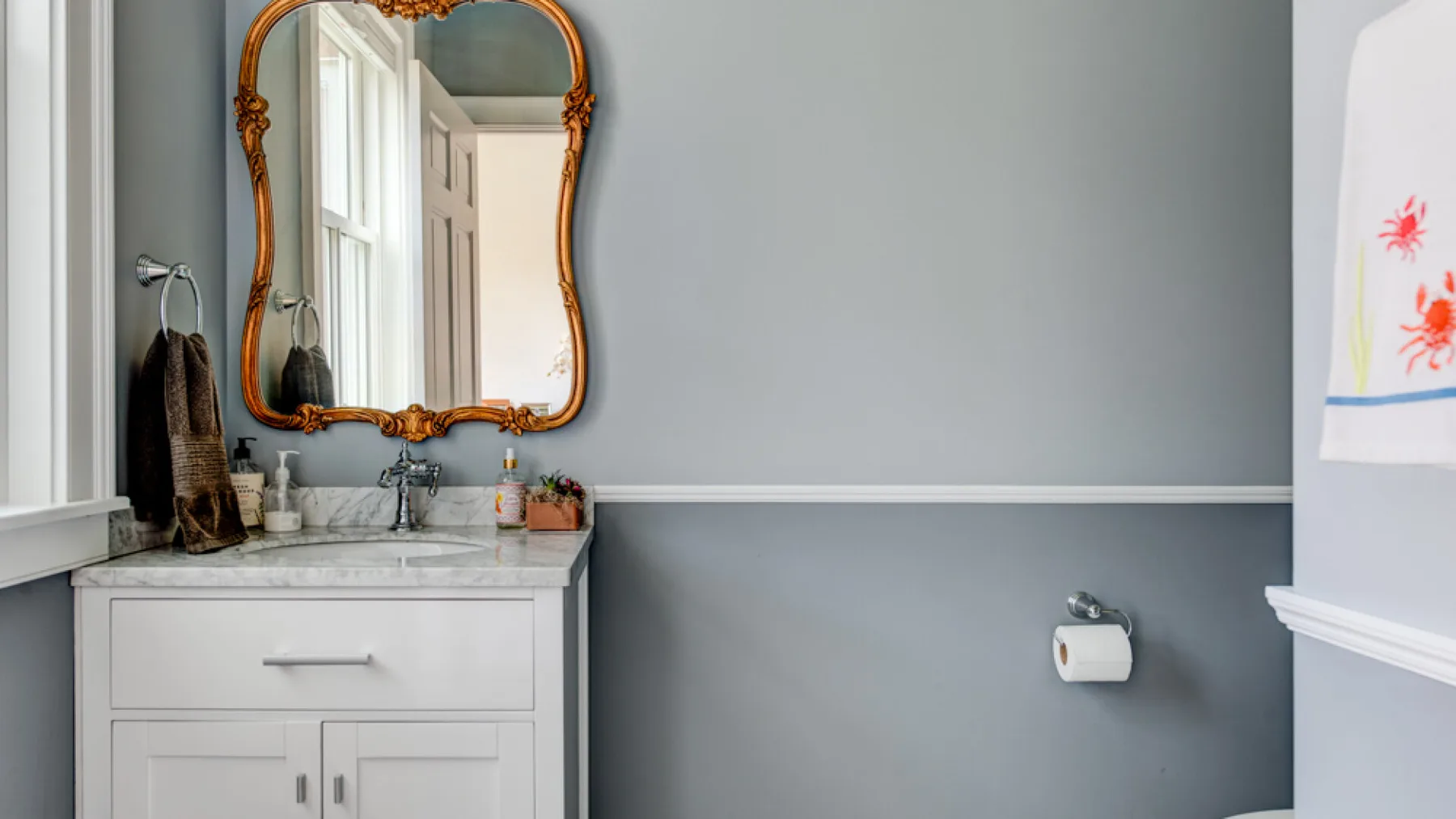 A bathroom vanity with a sink and ornate mirror against gray walls.