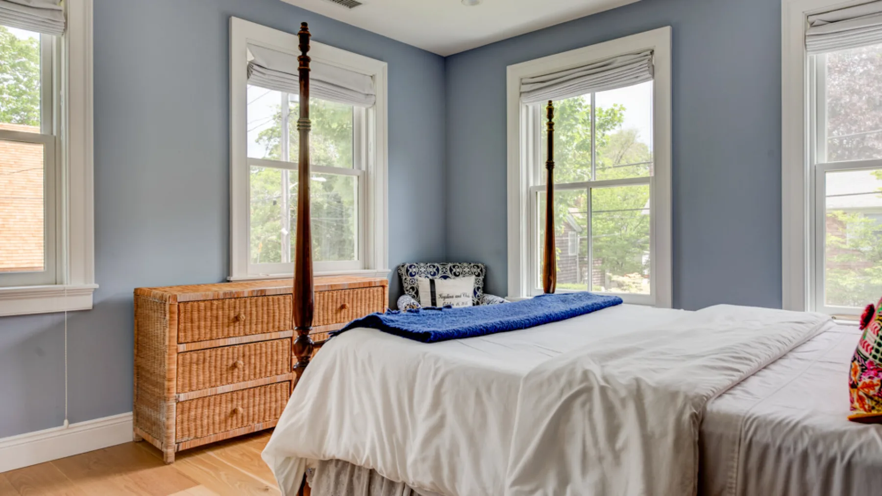 A bedroom with a bed, a wooden dresser, and several windows.