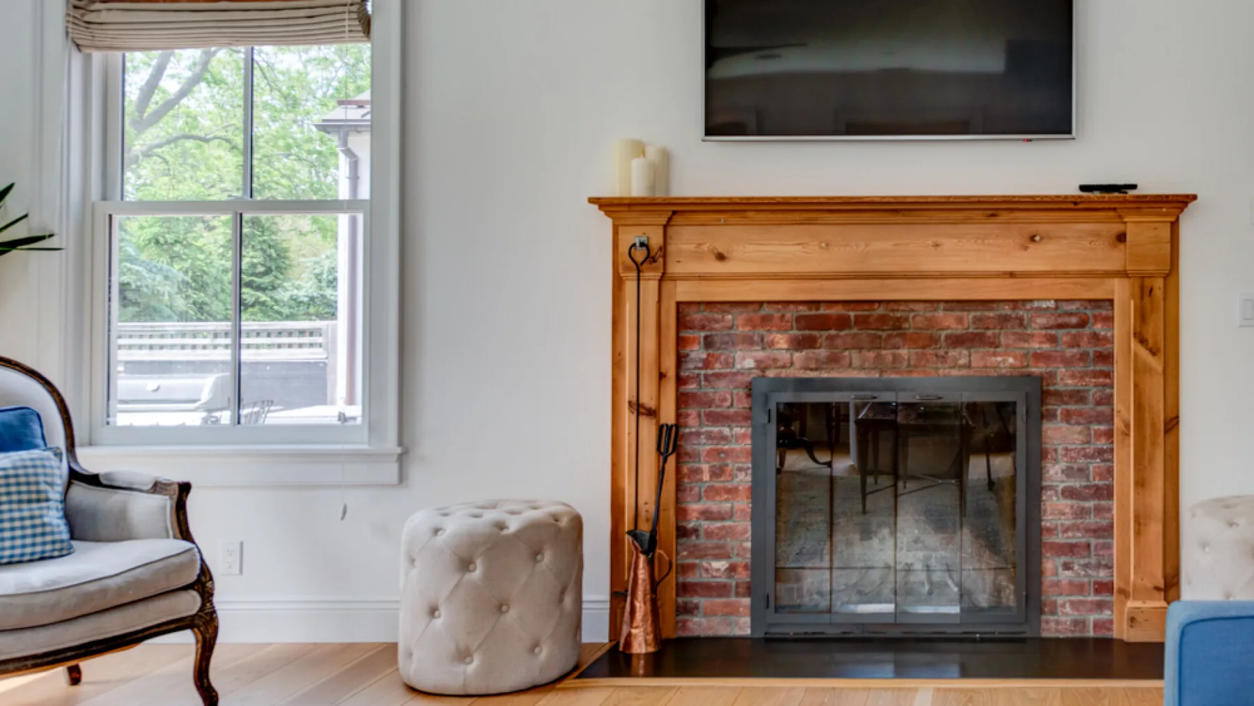 A living room with a brick fireplace, wall-mounted television, and seating by a window.