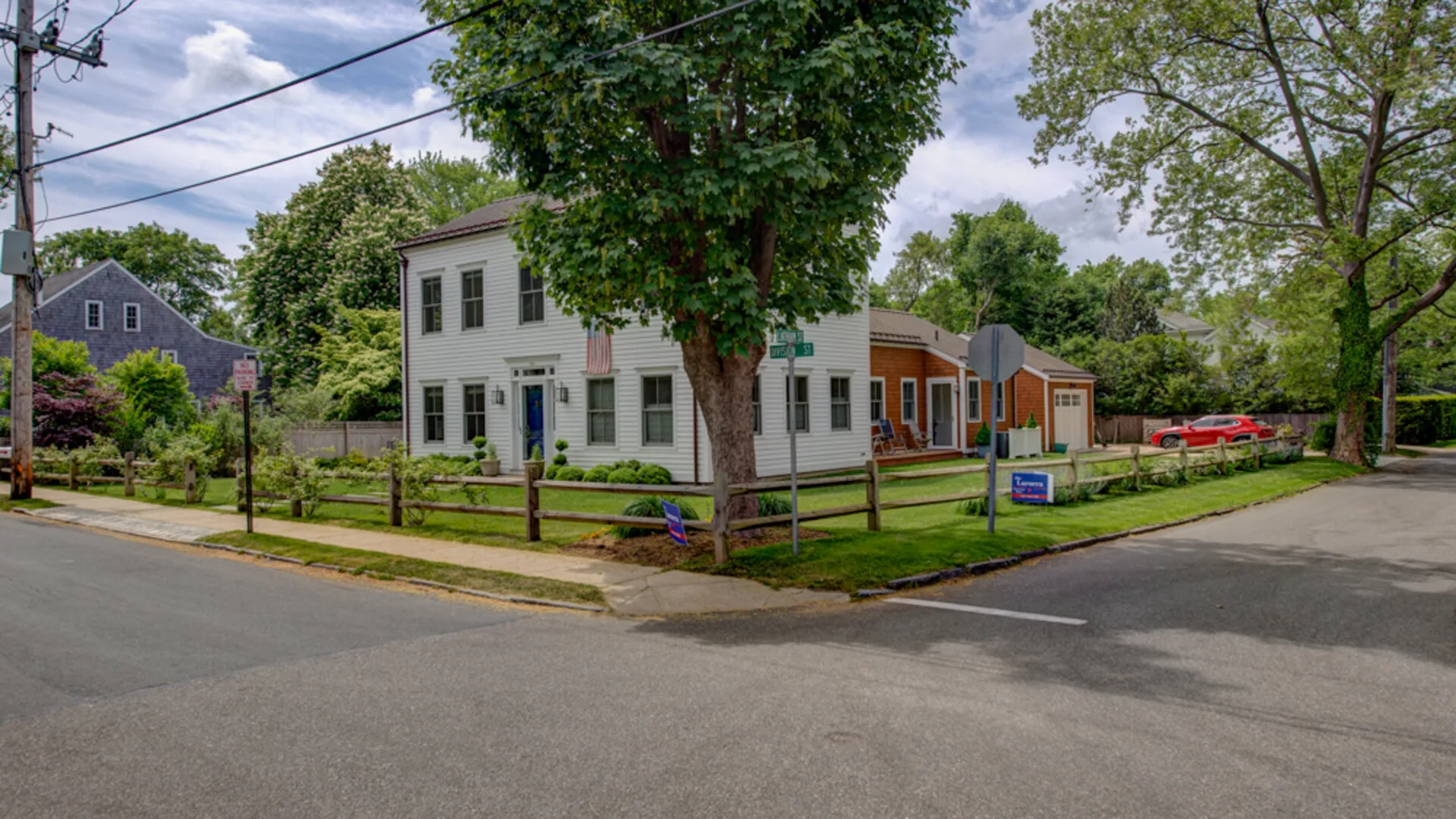 A white two-story building stands beside a tree-lined street.