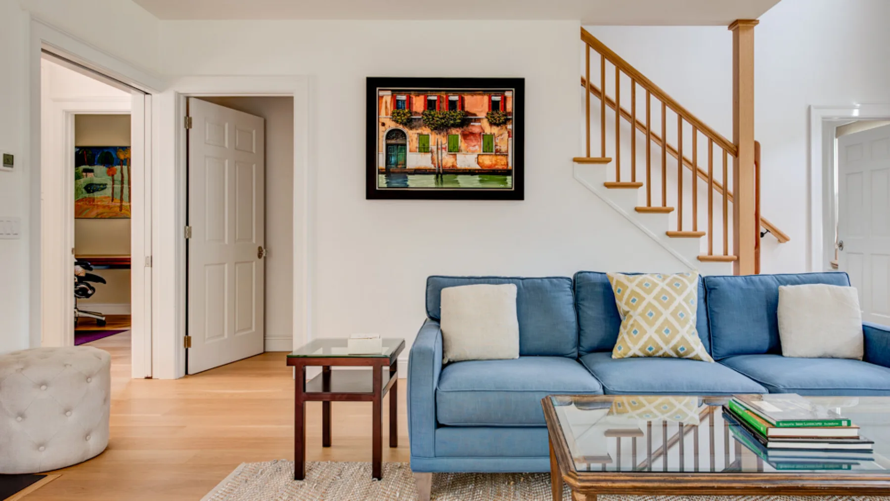 A living room with blue seating, a glass coffee table, and a staircase.