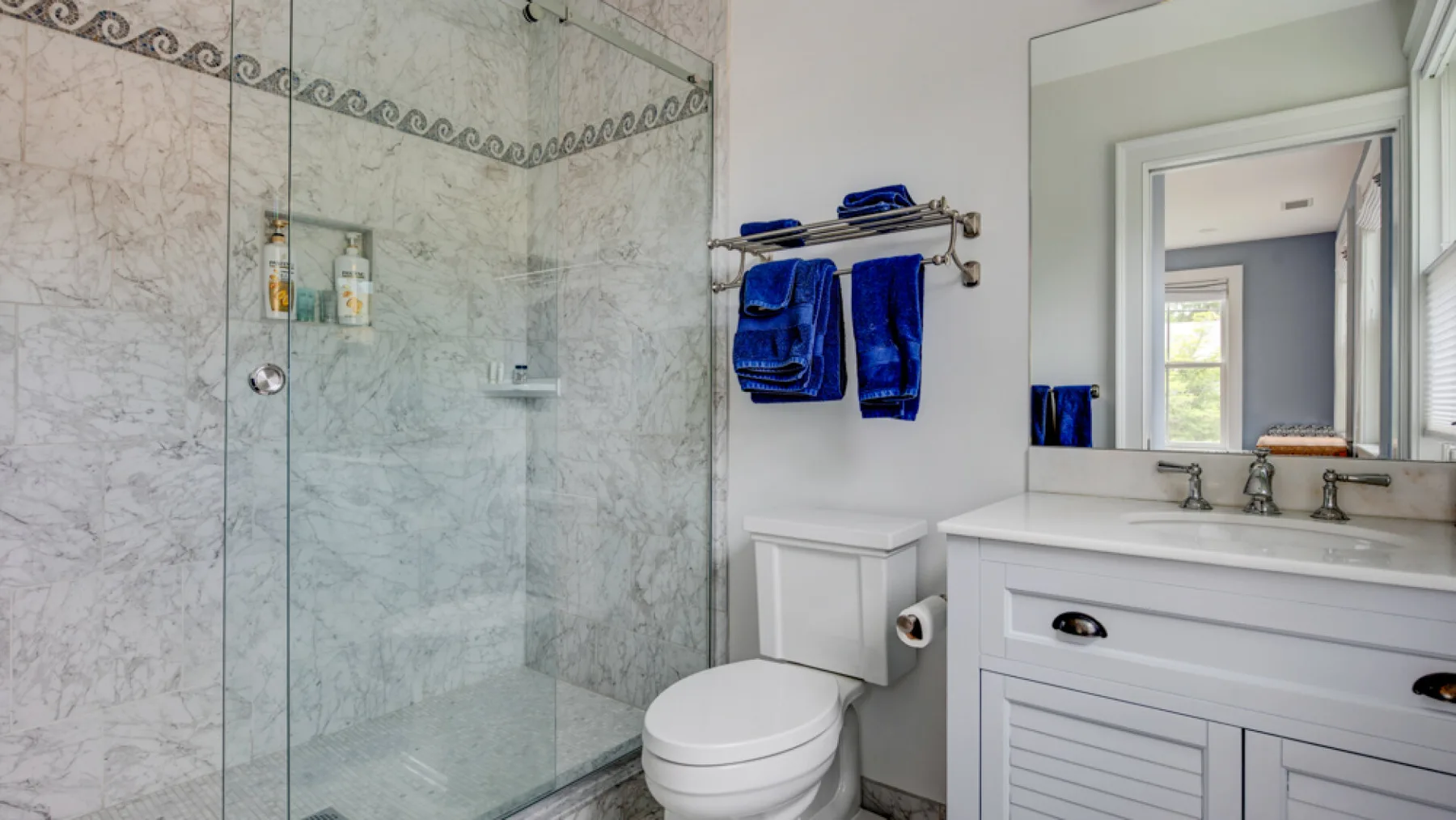 A bathroom with a glass shower, toilet, and sink beneath a large mirror.