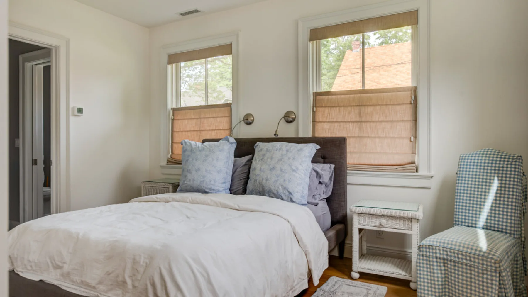 A bedroom with a bed beneath two windows and a patterned chair nearby.
