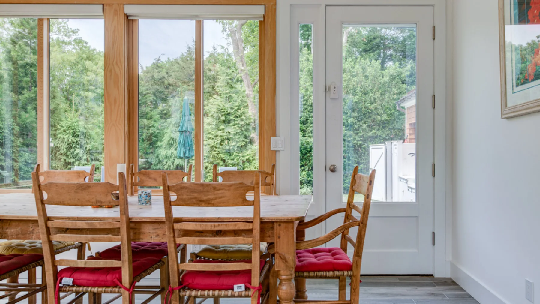 A dining area with a wooden table and red-cushioned seating beside large windows.