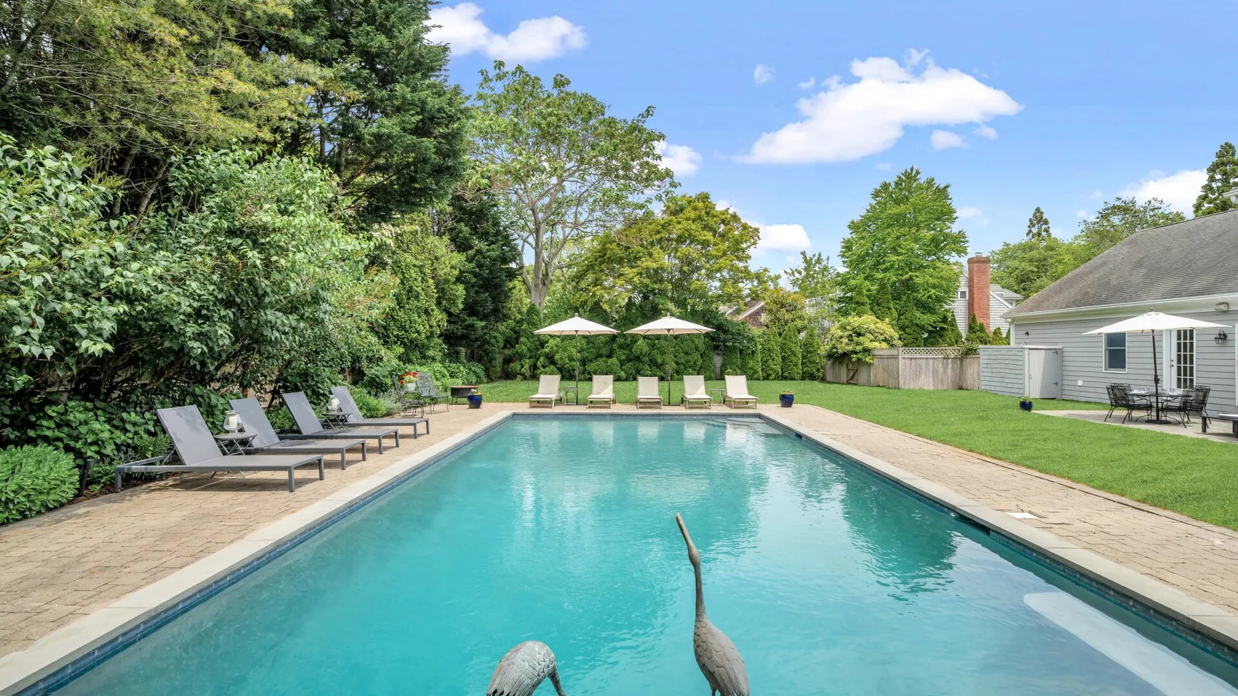 Piscina al aire libre rodeada de una terraza pavimentada, asientos y árboles frondosos.