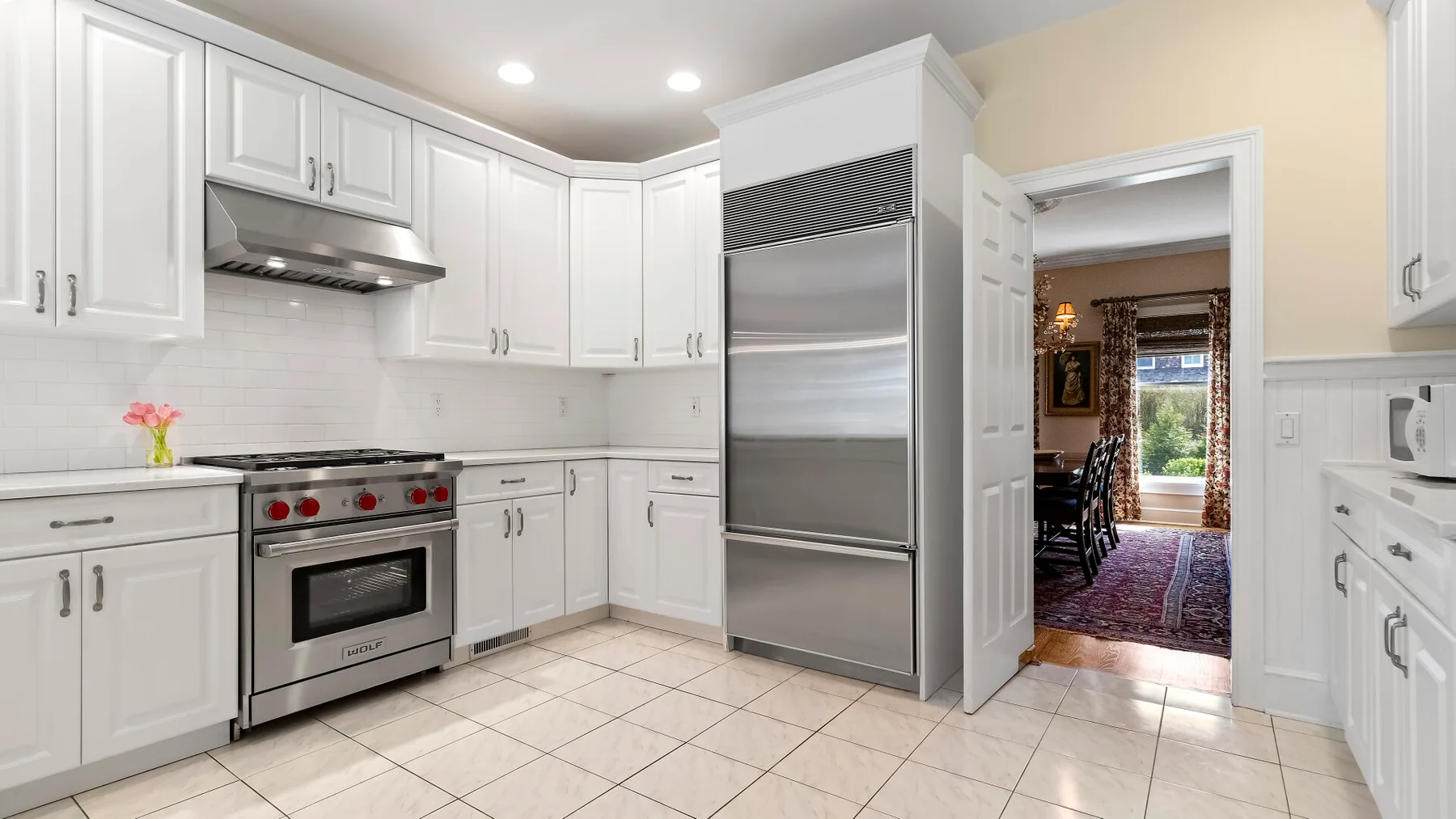 Una cocina blanca y luminosa con gabinetes, una estufa y un refrigerador grande de acero inoxidable.