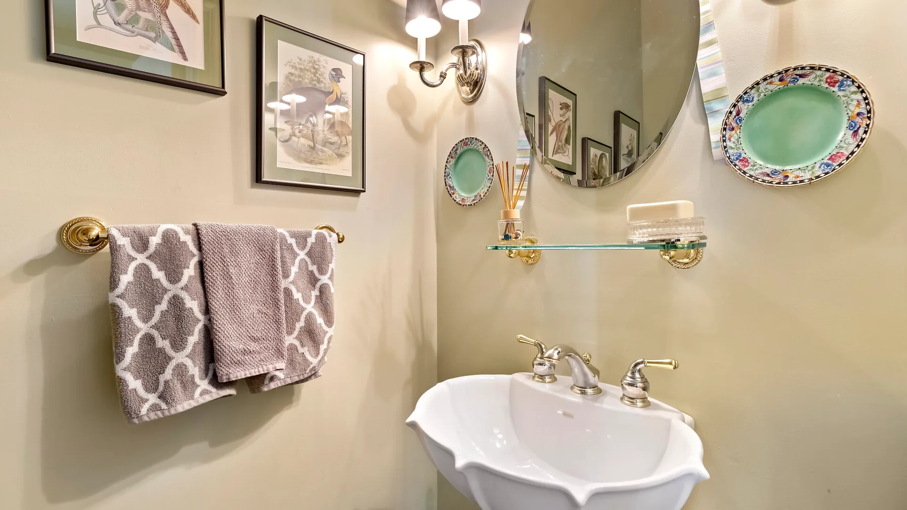 Un lavabo de baño con un fregadero blanco, espejo de pared y cuadros enmarcados.