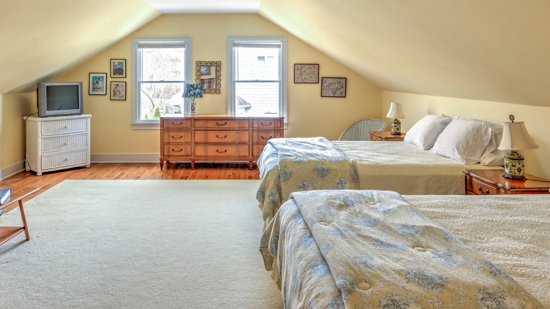Un dormitorio abuhardillado con dos camas y una cómoda bajo las ventanas.