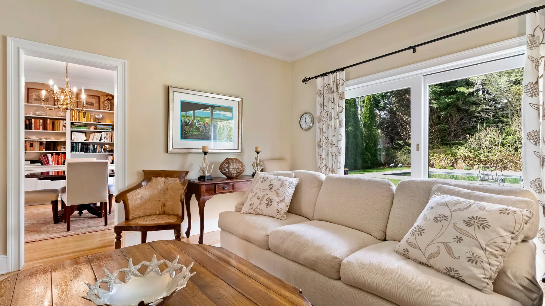 Una sala de estar con un sofá beige y grandes ventanas con vista a la vegetación.