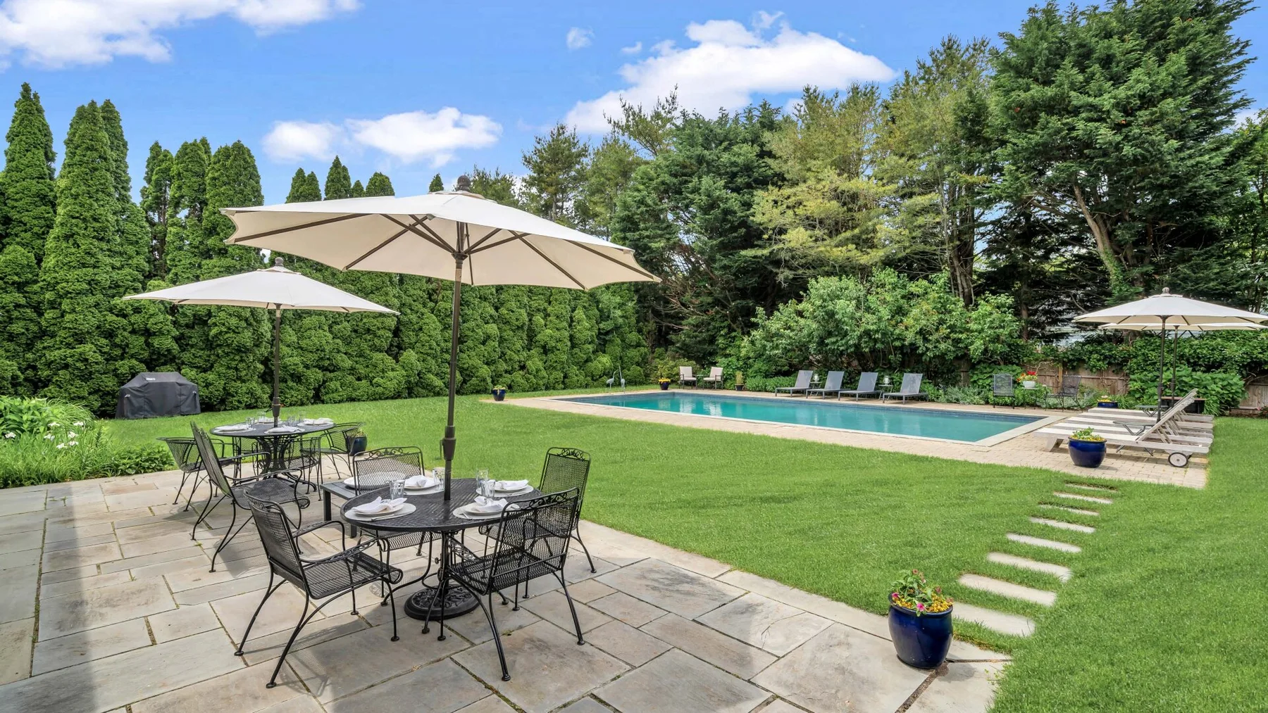 Un patio exterior con asientos de comedor da a una piscina y un jardín ajardinado.