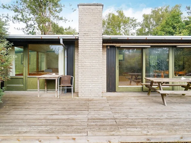 Una casa da a una terraza de madera, con grandes ventanas y asientos al aire libre.