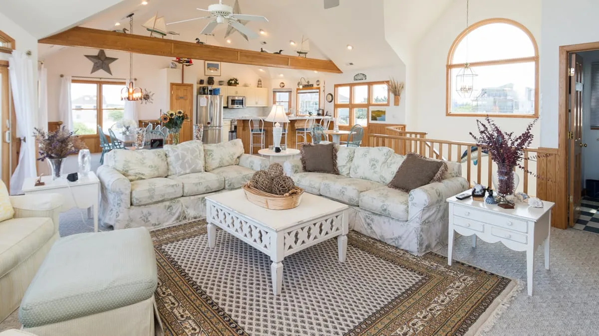 A bright living room with pale seating arranged around a coffee table and patterned rug.