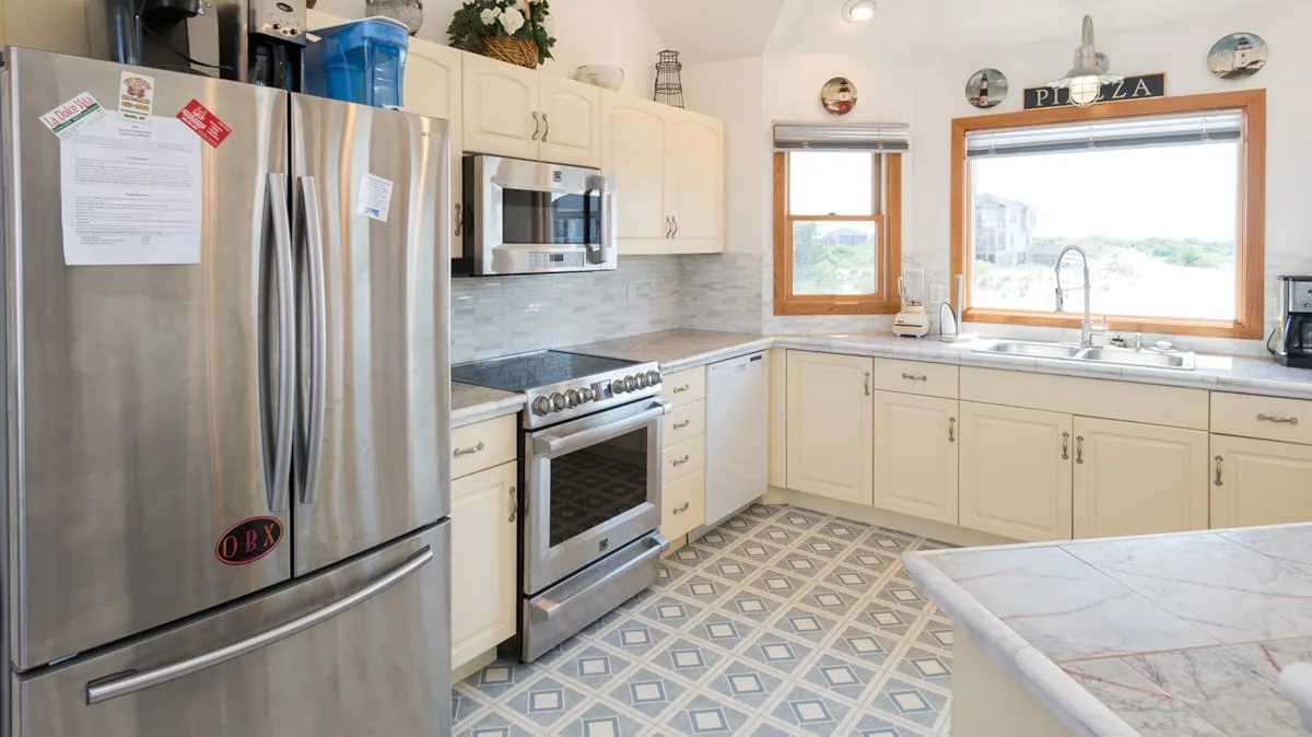 A bright kitchen with cream cabinets, stainless steel appliances, and patterned flooring.
