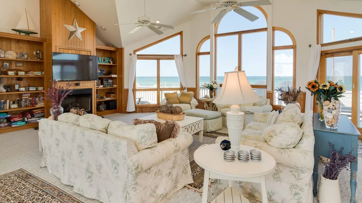 A bright living room with seating arranged around a coffee table and large ocean-facing windows.