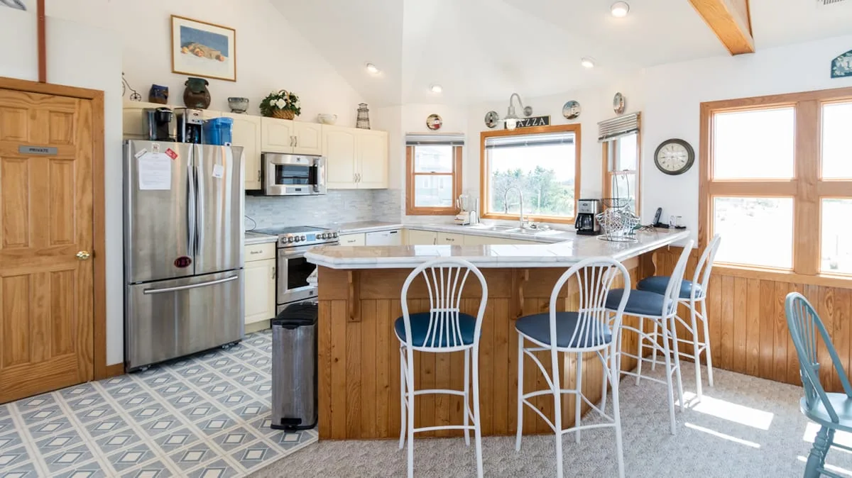 A bright kitchen with a central island, bar seating, and large windows.