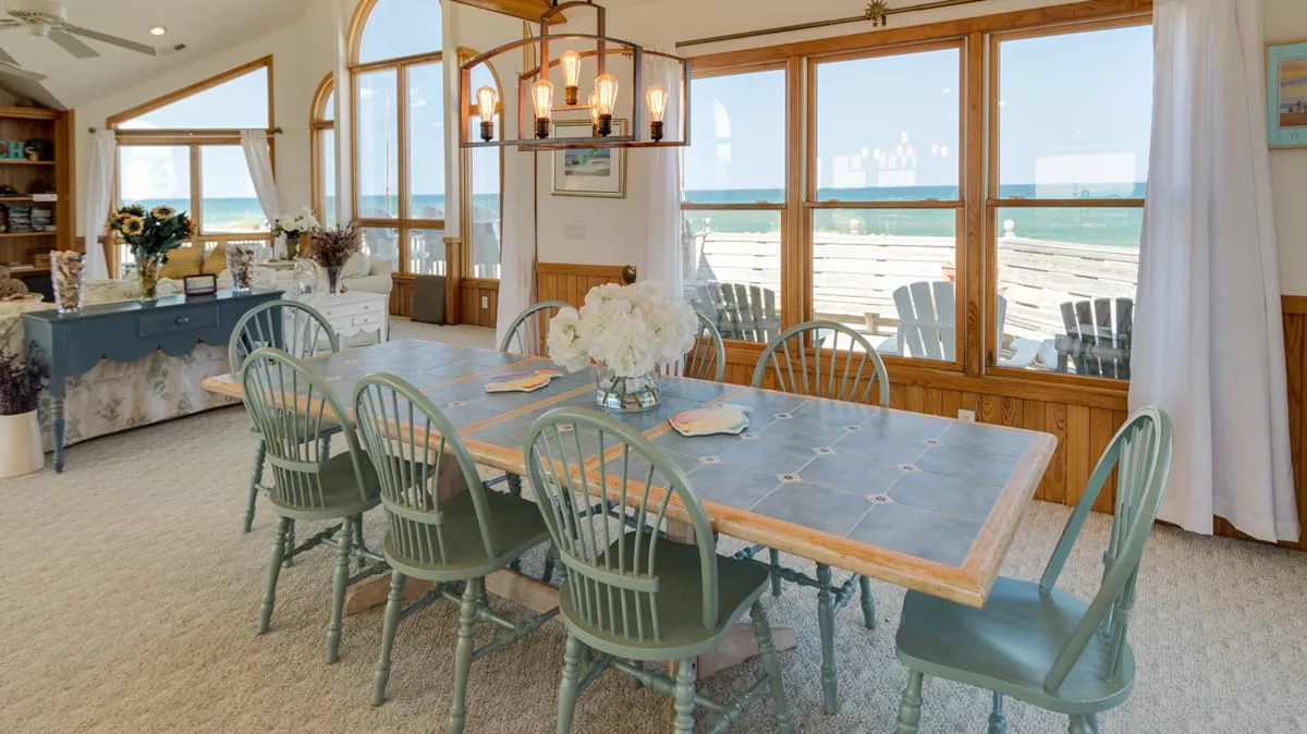 A dining room with a long table and large windows overlooking the water.