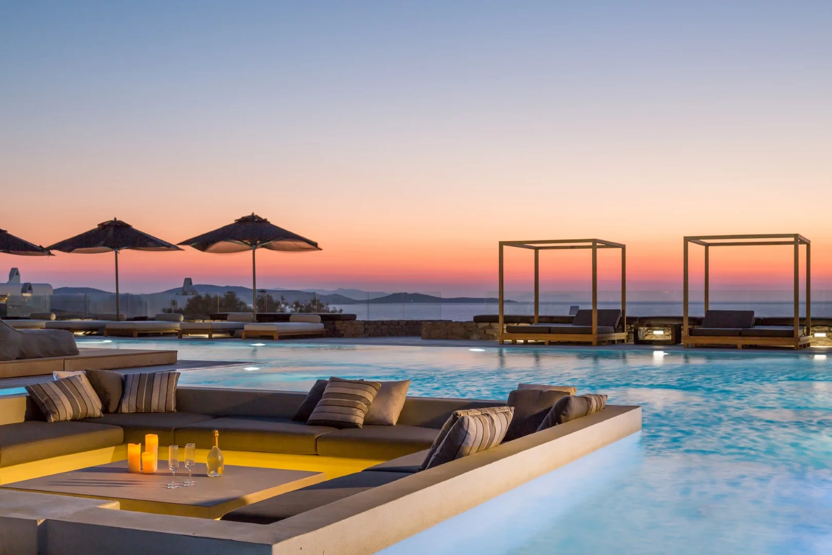 A swimming pool and lounge seating overlook the water at sunset.
