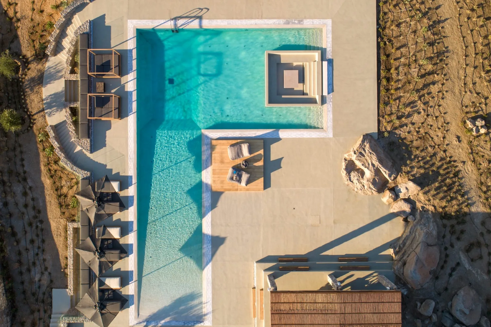 Aerial view of a swimming pool surrounded by a paved deck and lounge seating.