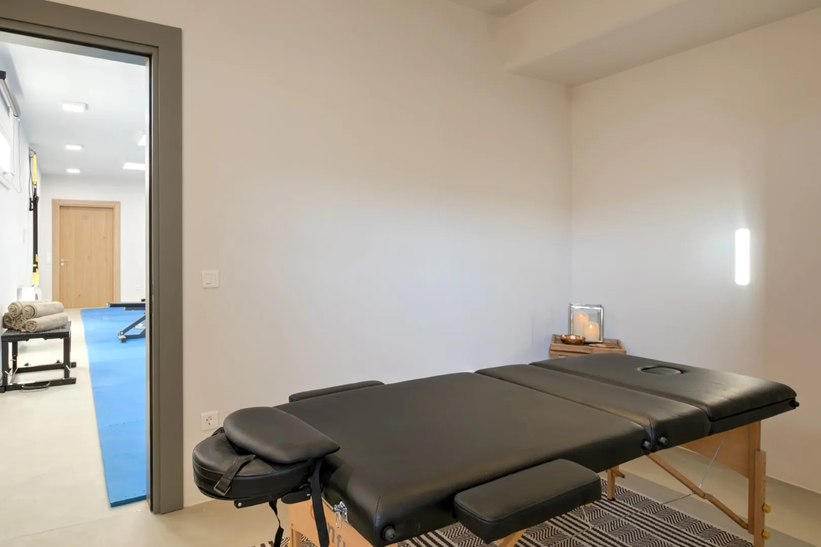 A treatment room with a padded massage table and wall lighting.