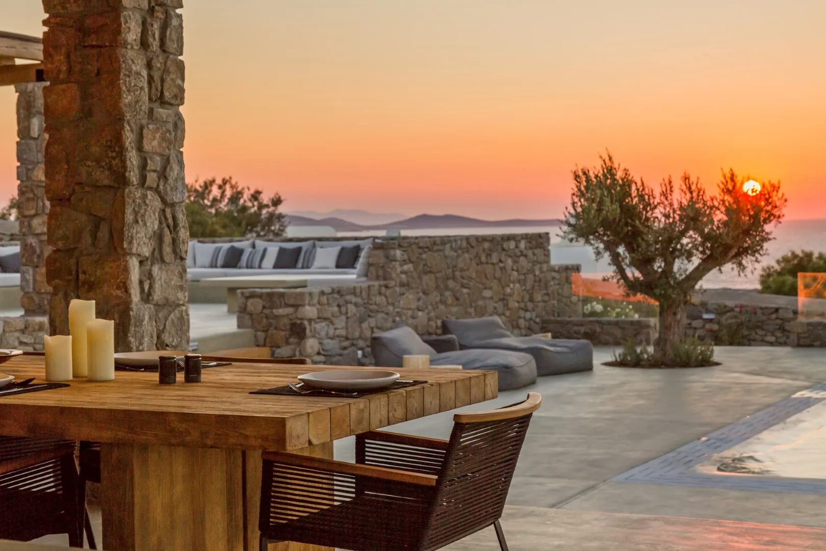 An outdoor dining area overlooks a stone terrace and sunset.