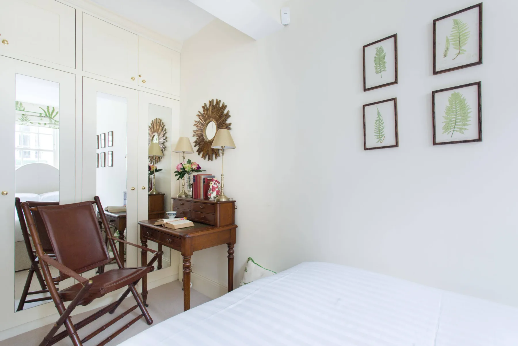 Un dormitorio con una cama blanca, un escritorio de madera y láminas botánicas enmarcadas.