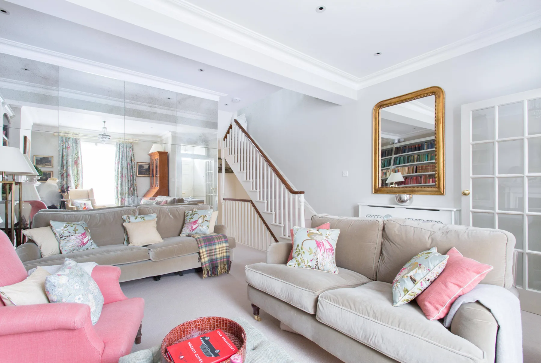 Una sala luminosa con asientos neutros, detalles rosas y una escalera.