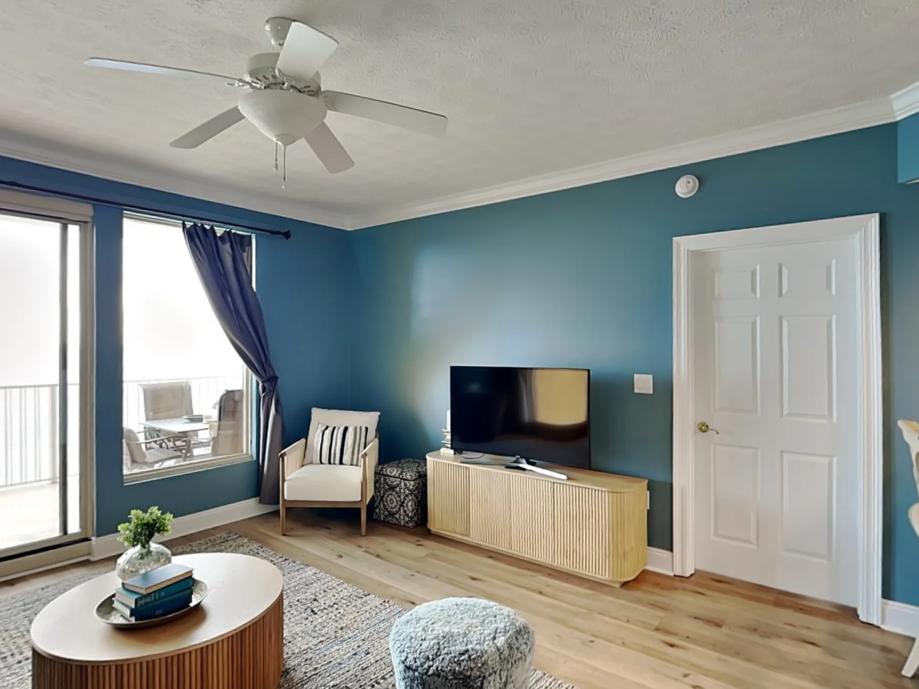 A living room with a television on a wooden console beside bright windows.